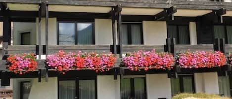 A multi-story building with balconies, a covered outdoor seating area, and a stone wall.