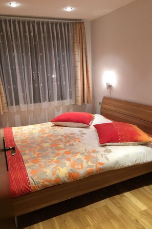 Ein Bett mit floralem Überwurf, zwei roten Kissen und einem hölzernen Kopfteil.