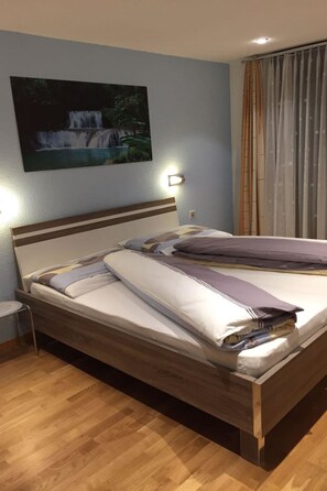 Ein ordentlich bezogenes Bett mit Holz-Kopfteil, einer Wandleuchte und einem Gemälde eines Wasserfalls.