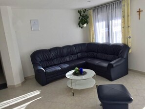 Ein Wohnzimmer mit einem schwarzen Ledersofa, einem kleinen runden Couchtisch und einem weißen Boden.