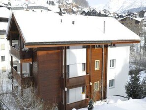 Ein zweistöckiges Holzhaus mit einem Balkon, umgeben von schneebedeckten Bergen.
