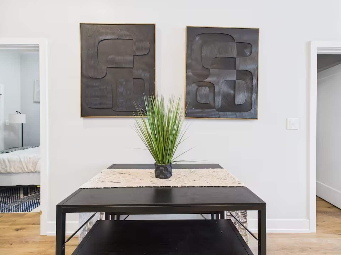 Une pièce avec une table noire, une plante en pot et deux tableaux abstraits accrochés au mur.
