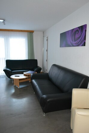 Ein modernes Wohnzimmer mit einer schwarzen Couch, einem beigen Sessel und einem kleinen Holztisch.