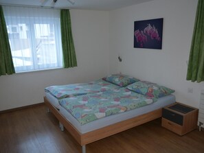 Ein Schlafzimmer mit einem hölzernen Bett, grünen Vorhängen, einem Fenster und einer Wandleuchte.
