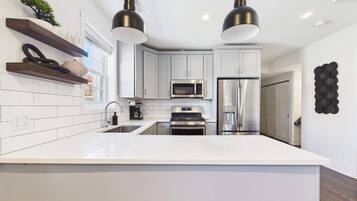 Une cuisine moderne avec des meubles blancs, des appareils en acier inoxydable et des luminaires suspendus.