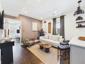 A modern living room with a sofa, chairs, a coffee table, and a kitchen area with a counter and stools. - Peaceful Boho Retreat | Free Private Parking (Chicago)