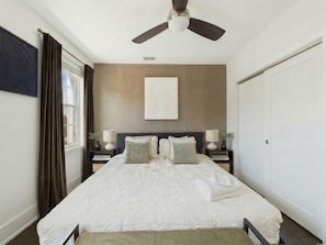 Un dormitorio con cama, ventilador de techo, ventana con cortinas y puerta.