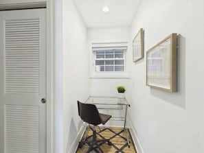Un pasillo con una puerta, un ventanal, una silla y cuadros en la pared.
