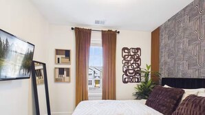 Una camera d'albergo con un letto, una TV a schermo piatto, una finestra con tende e una parete con motivo geometrico.