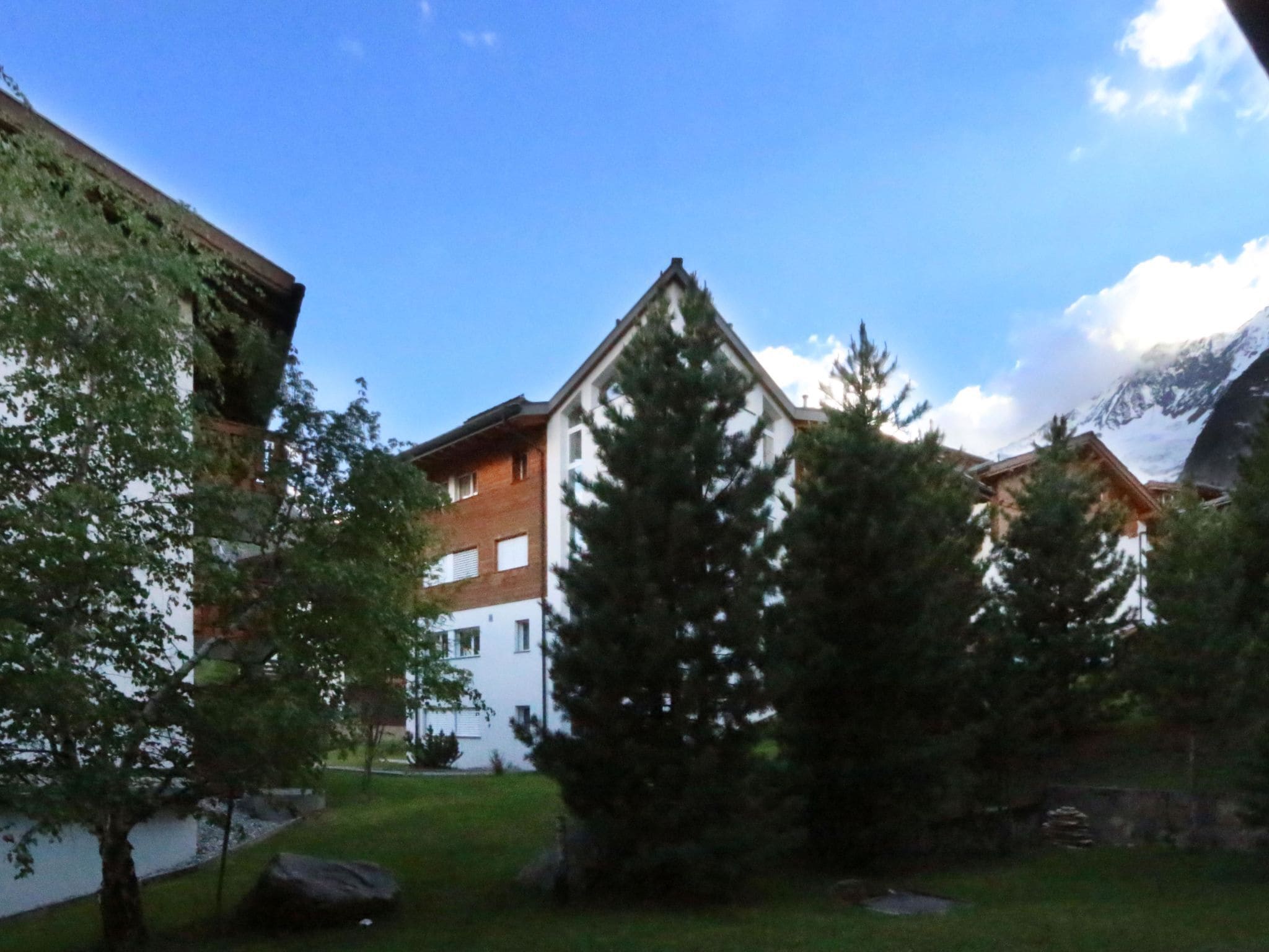 Ein Gebäude mit einem geneigten Dach, umgeben von Bäumen und blauem Himmel.