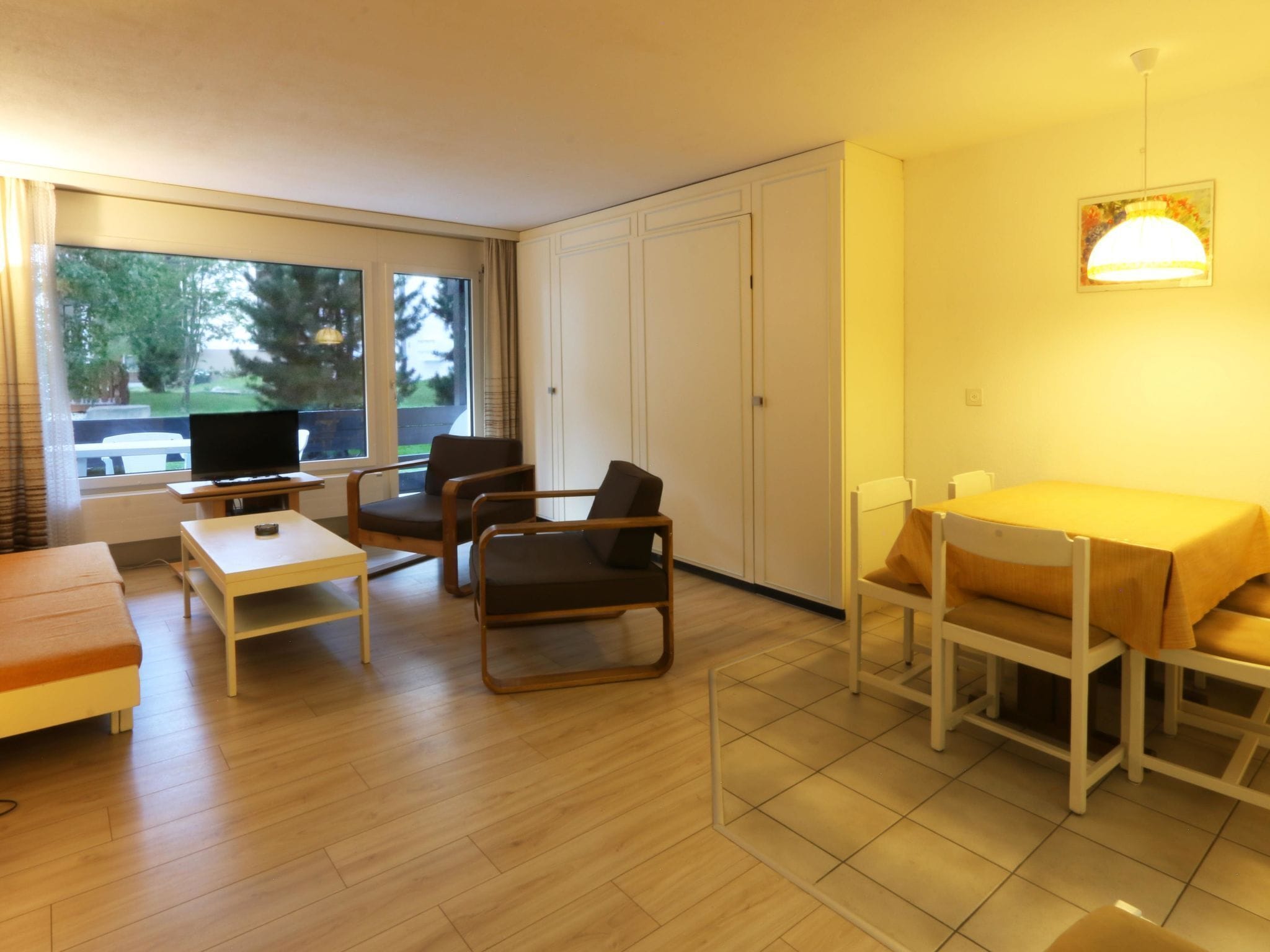 A furnished living room with a sofa, chairs, a table, and a television.