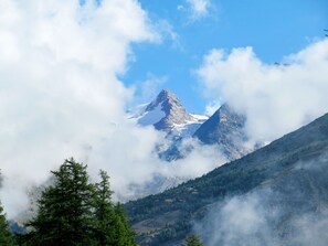 Eine Berglandschaft mit schneebedeckten Gipfeln, dichtem Wald und Wolken.