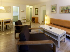 A modern living room with a sofa, a dining table, and chairs. There is a kitchen area in the background. - Amici Appartement/Fewo 4-Bettwohnung Nr. 4 by Interhome (Saas-Fee)