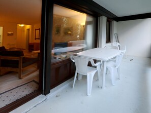 Ein Essbereich mit einem weißen Tisch und Stühlen, einer Holzbank und Blick durch eine Glastür in einen Raum mit einem Bett und einer Lampe.