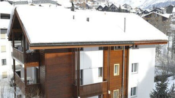 Ein zweistöckiges Holzhaus mit einem Balkon, umgeben von schneebedeckten Bergen.