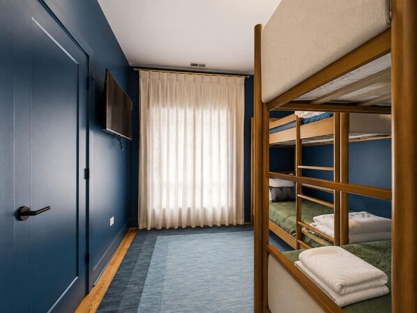 A room with a bunk bed, a door, a flat-screen TV, and a window with curtains.