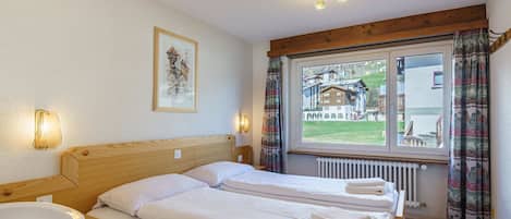 Une chambre d’hôtel avec deux lits, une tête de lit en bois, une table de chevet avec un lavabo blanc et une fenêtre avec des rideaux.