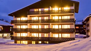 Ein mehrstöckiges Hotel mit Balkonen, verschneiter Umgebung und beleuchteten Fenstern.
