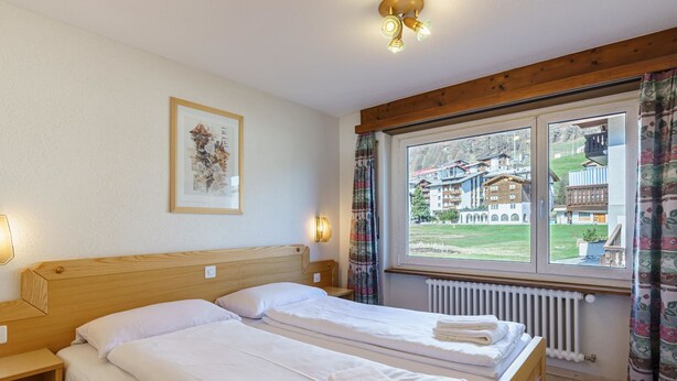 Ein Hotelzimmer mit zwei Betten, einem Fenster mit Blick auf Gebäude und einem gerahmten Bild an der Wand.