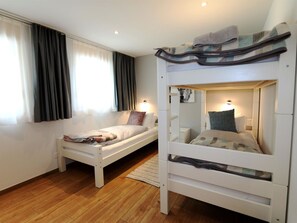 A room with a bunk bed, a single bed, a window with curtains, and a wall-mounted light fixture. - Derby Appartement/Fewo Derby 2 by Interhome (Saas-Fee)