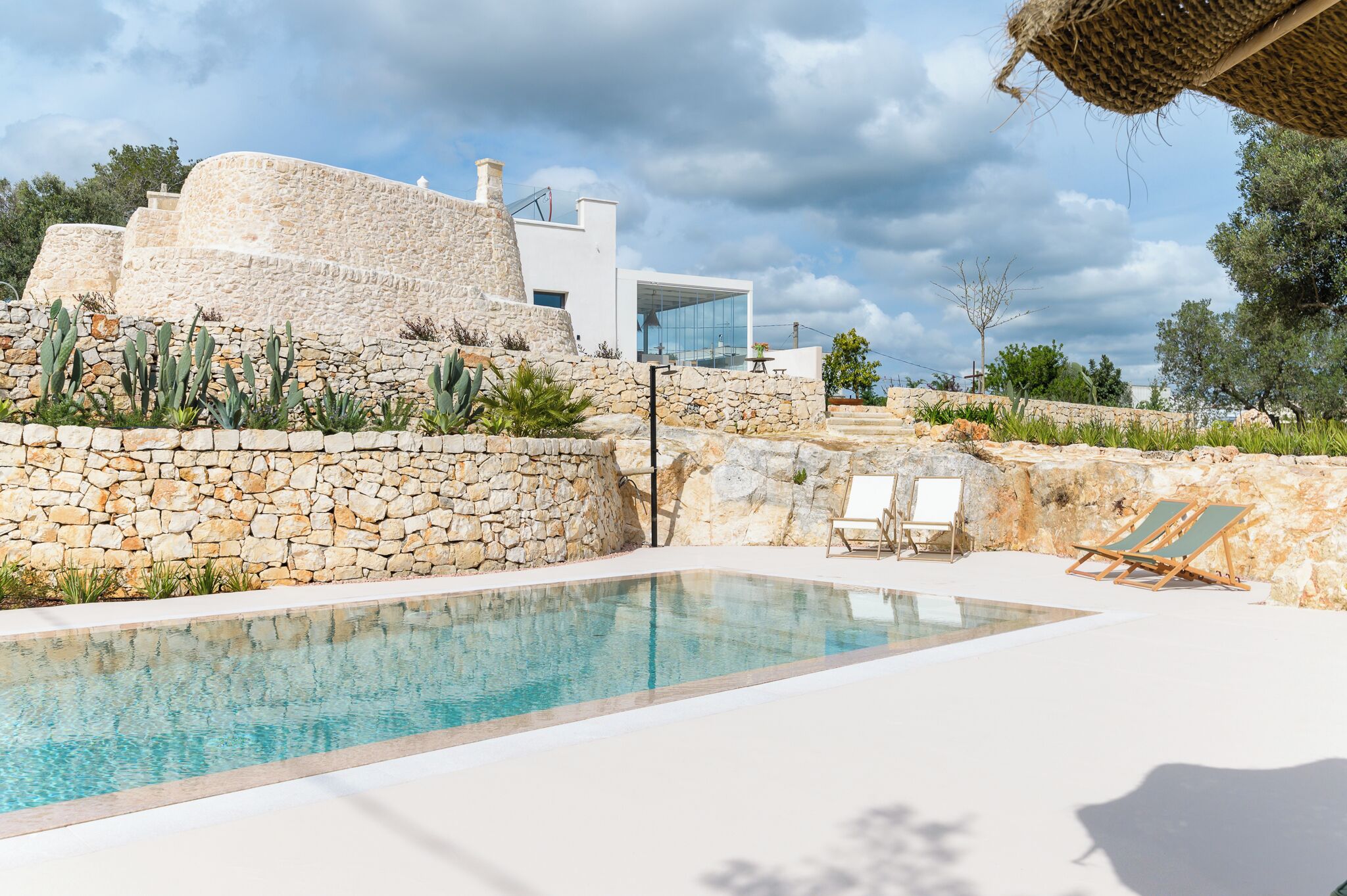 A pool area with stone walls, a modern building, and a clear sky.
