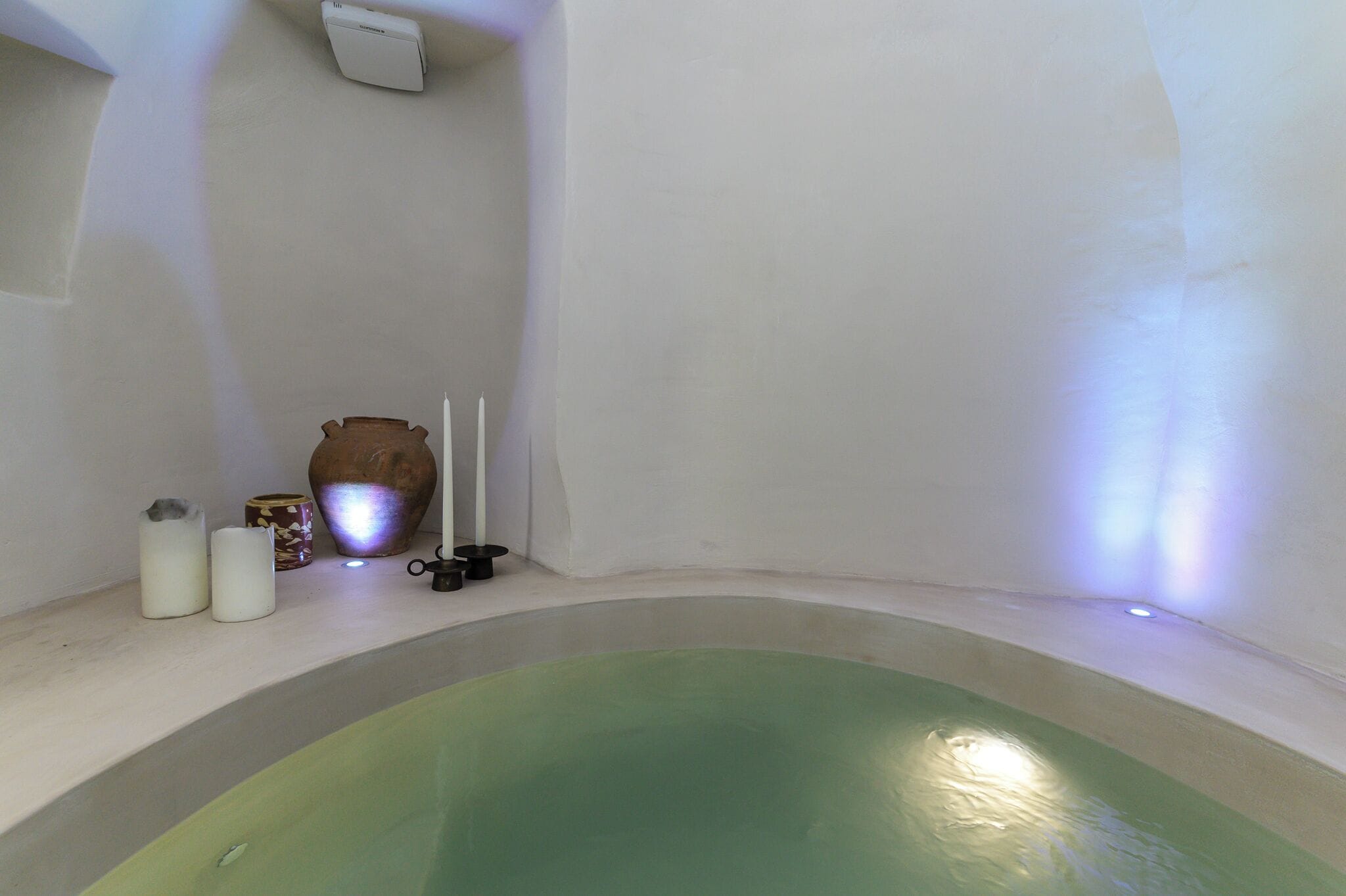 A spa room with a green bathtub, a white wall, and a small shelf with candles and a vase.