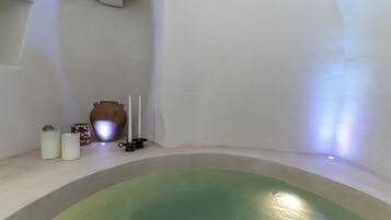 A spa room with a green bathtub, a white wall, and a small shelf with candles and a vase.