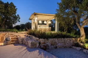 Ein Essbereich im Freien mit Steinwänden und einer Pergola, inklusive Tisch und Stühlen.