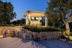 Zona pranzo all'aperto con pareti in pietra, una pergola, un tavolo e sedie.