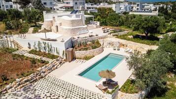 A rooftop pool area with a view of the cityscape, surrounded by greenery and stone structures.