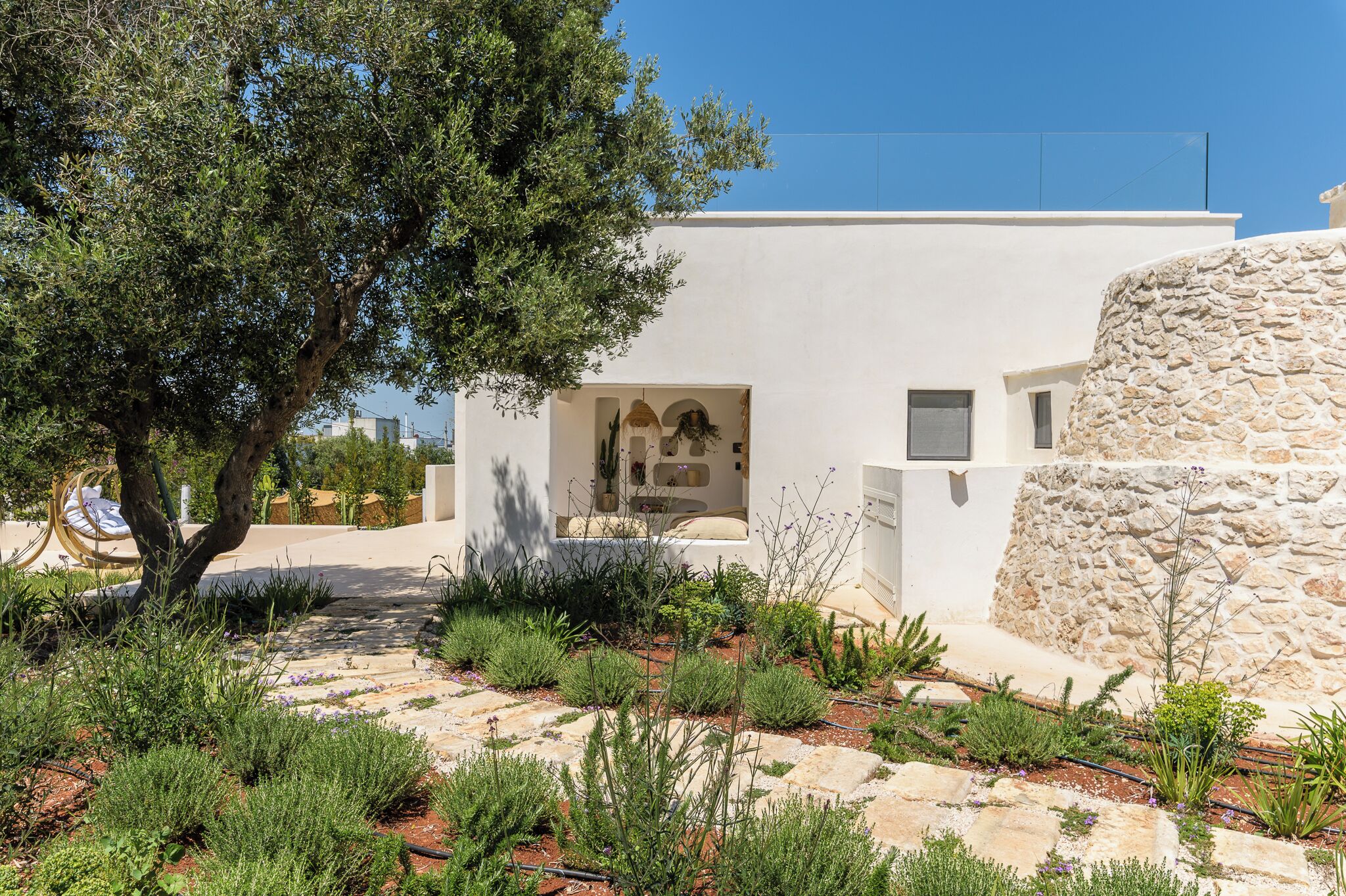 A modern building with a stone facade, a garden with various plants, and a clear sky.
