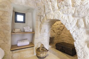 Una habitación con paredes de piedra, una estantería con toallas dobladas y una cesta de mimbre.