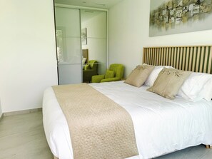 A modern bedroom with a large bed, a green armchair, and a glass door closet. - Luxurious villa with ocean views near Benidorm for 6 to 8 people (Finestrat)