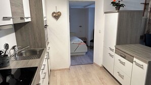 Eine kompakte Küche mit Spüle, Herd und Schränken. Ein Bett ist im angrenzenden Raum zu sehen.