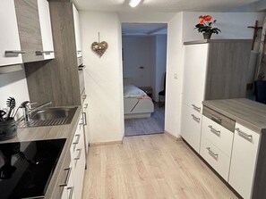 Cocina compacta con pileta, cocina y alacenas. Se ve una cama en la habitación contigua.