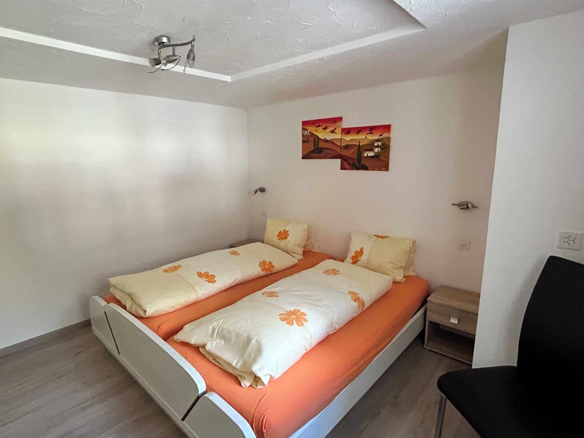 Une petite pièce propre, avec un lit, une chaise et une table de chevet.