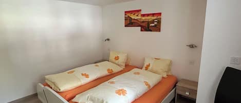 Una habitación pequeña y limpia con una cama, una silla y una mesita de noche.