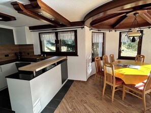 A modern kitchen with a central island, wooden dining table with chairs, and large windows with curtains. - Sunstar Appartement/Fewo 8-Bettwohnung Nr. 41 by Interhome (Saas-Grund)