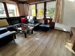 Un salon moderne avec un canapé en cuir noir, une table basse en verre et un plancher en bois.