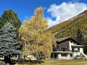 A two-story chalet with a balcony, surrounded by trees and a mountainous backdrop. - Sunstar Appartement/Fewo 8-Bettwohnung Nr. 41 by Interhome (Saas-Grund)