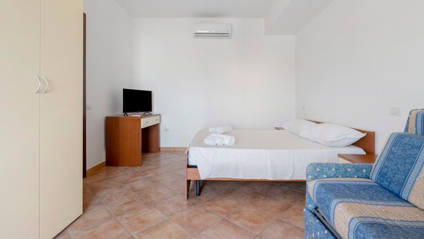 Un dormitorio con una cama, un televisor sobre un mueble de madera, una silla y un equipo de aire acondicionado en la pared.