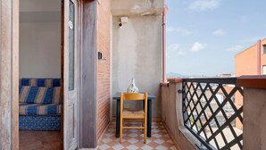 Un balcón con piso a cuadros, una silla de madera, una mesita y un sofá azul estampado.