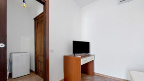 Una habitación con un escritorio de madera, televisor, refrigerador blanco y una puerta que da a otra habitación.