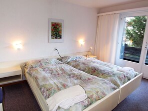 A double bed with floral bedding, a bedside table, a wall-mounted lamp, and a window with curtains. - Amici Appartement/Fewo 4-Bettwohnung Nr. 2 by Interhome (Saas-Fee)
