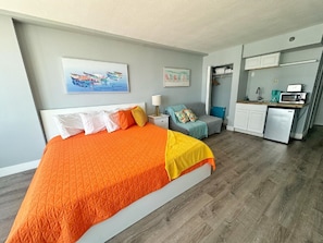 Une chambre avec un grand lit, une petite kitchenette et un canapé gris.