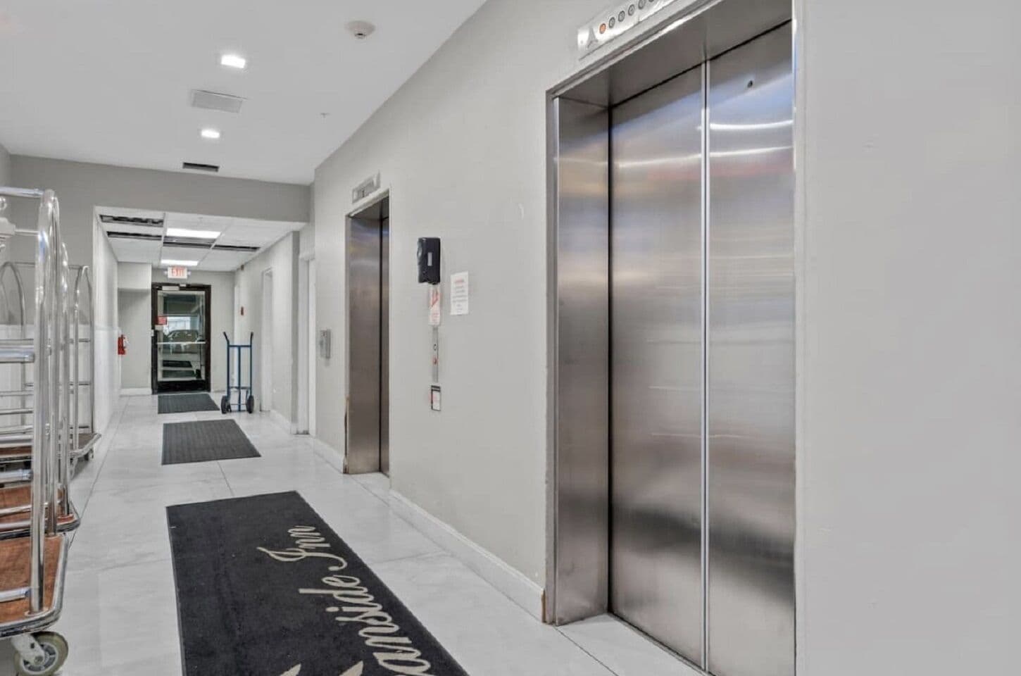 Ein moderner Hotelkorridor mit klarem, minimalistischem Design, der ein zentrales Aufzug und einen deutlichen Weg zum Eingang zeigt.