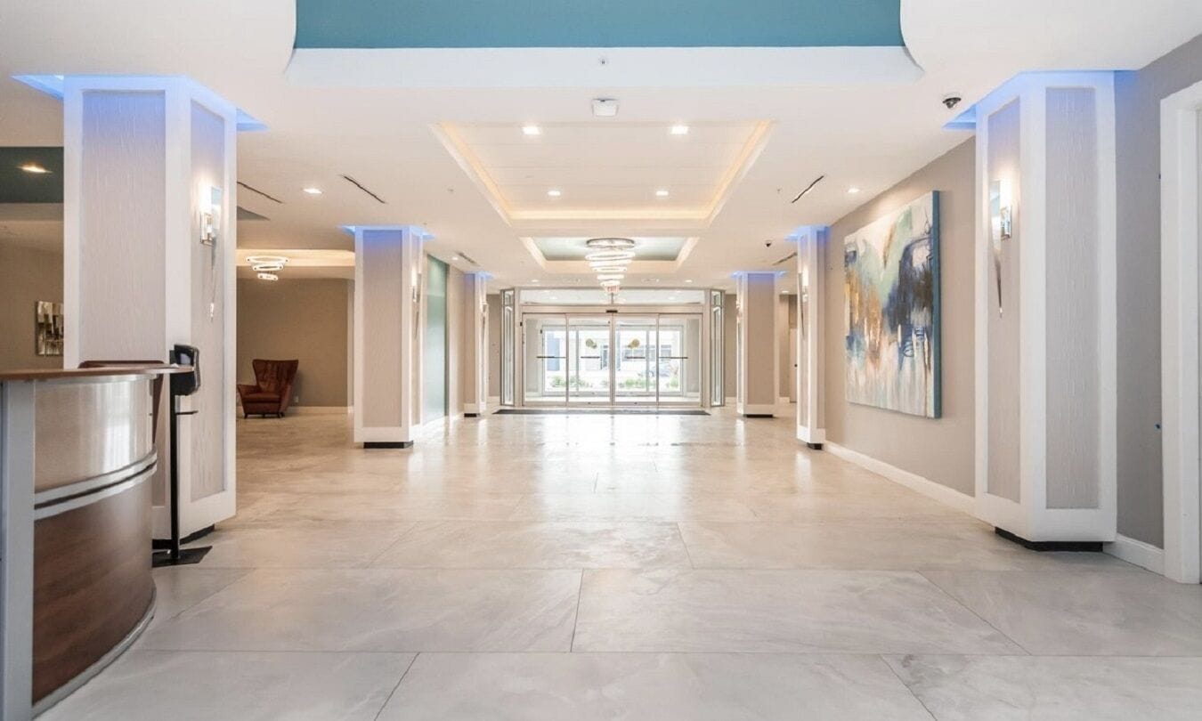 Ein geräumiger Hotelkorridor mit modernem Design, der eine zentrale Leuchte, einen Empfangsbereich mit Theke und Kunstwerke an den Wänden zeigt.