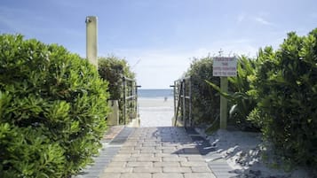 Ein gepflasterter Weg führt zu einem Strand, auf dem ein Schild das Tragen von Hotelmöbeln zum Strand verbietet.