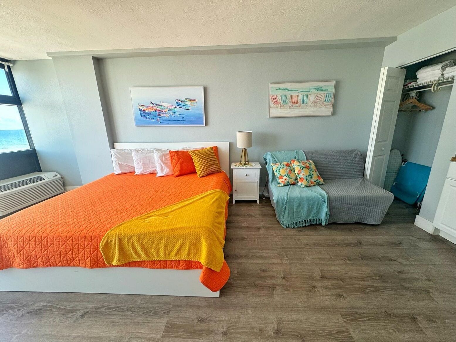 Ein Schlafzimmer mit einem großen Bett, einem Nachttisch mit Lampe, einem grauen Sofa und zwei Wandbildern.