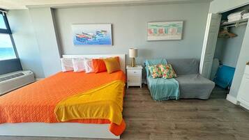 Ein Schlafzimmer mit einem großen Bett, einem Nachttisch mit Lampe, einem grauen Sofa und zwei Wandbildern.